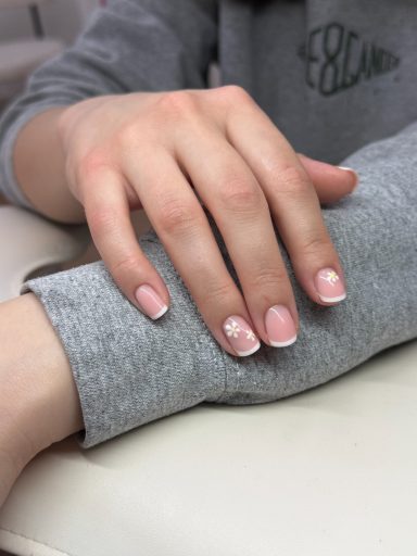 A hand with manicured nails featuring a French tip design rests on a grey fabric surface.