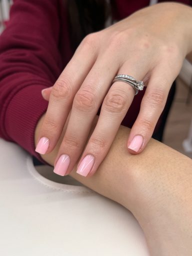 A hand with pink nails rests on another hand, adorned with a silver ring.