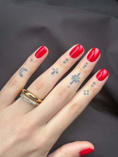 A hand with red nails adorned with various small tattoos, including stars and a crescent moon.