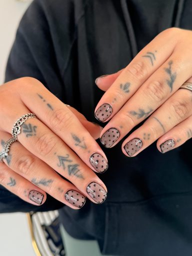 Hands with tattooed fingers showcasing decorative nail art and rings.