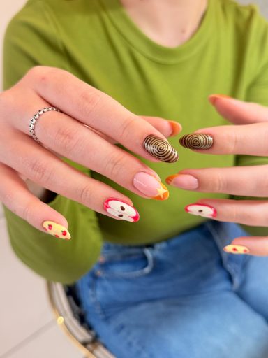 Colourful nail art featuring various designs on fingers, against a green top backdrop.