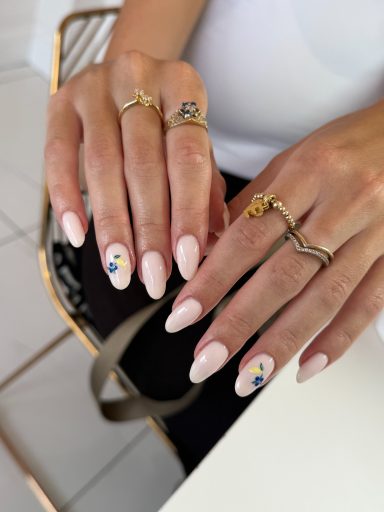 Well-groomed hands with long pink nails, featuring colourful floral designs and rings.