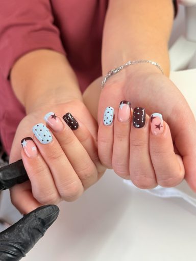 Two hands with stylish nails featuring blue, brown, and polka dot designs.