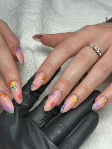 Manicured hands with pastel nails featuring floral designs and a glossy finish.