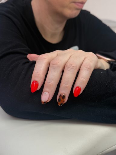 Close-up of a hand with red and patterned nails resting on a person's arm.